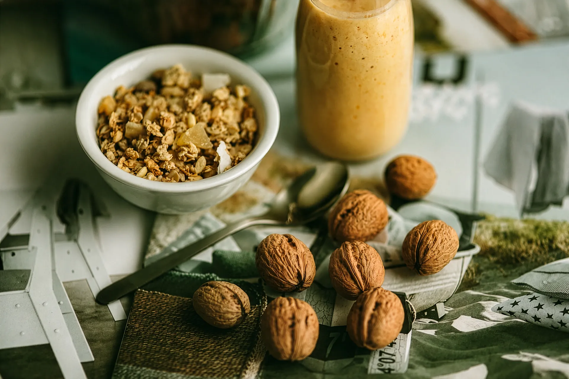 Schüssel mit Granola, ein Glas orangefarbener Smoothie und mehrere Walnüsse auf einem Tisch